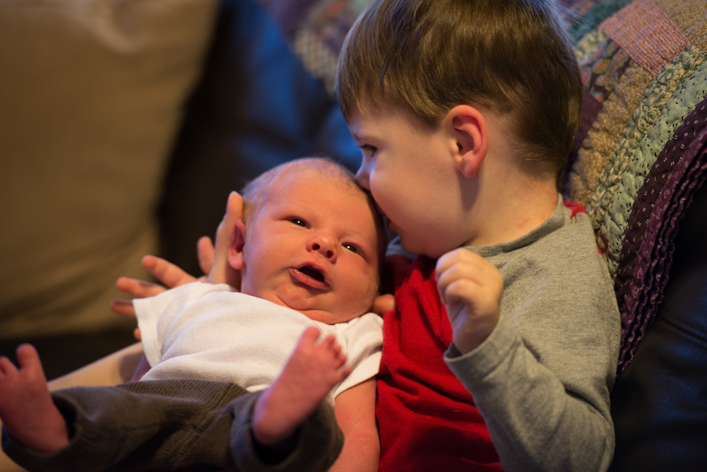 Ein Kind, das ein Baby hält, beide tragen Kleider in verschiedenen Farben, mit einem unscharfen Hintergrund.