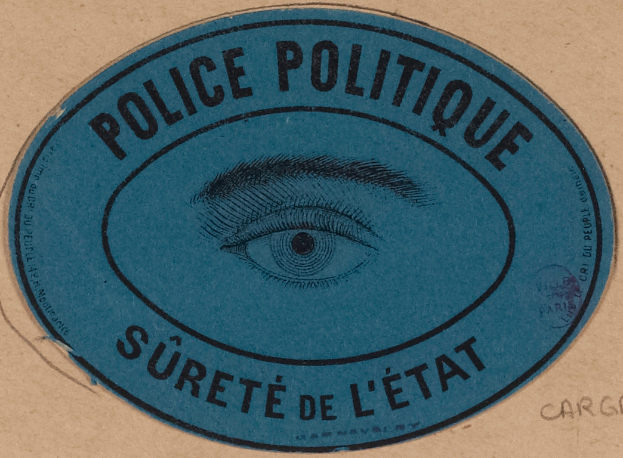 Ein brauner Karton mit einem blauen Aufkleber, auf dem "Polizei Politique Surete de L'Etat" und ein Auge in der Mitte steht.