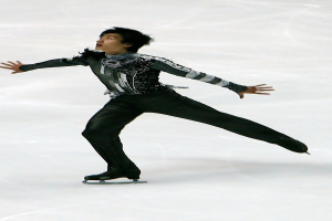 Männlicher Eiskunstläufer gleitet über eine Eisfläche in einem schwarzen Kleid und Schlittschuhen, führt eine Routine mit synchronisierten Arm- und Beinbewegungen aus.