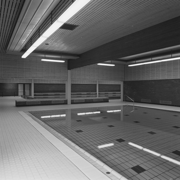 Innenpool mit klarem Wasser, gefliestem Boden, Wänden und Deckenbeleuchtung, umgeben von wenigen Gegenständen in einer friedlichen Umgebung.