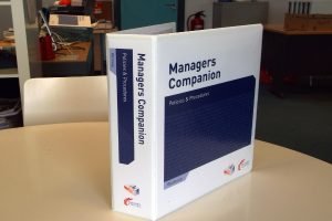 Ein Buch auf einem Tisch mit einem Stuhl dahinter, in der Nähe einer Tür, Feuerlöscher, Dateien und andere Gegenstände.