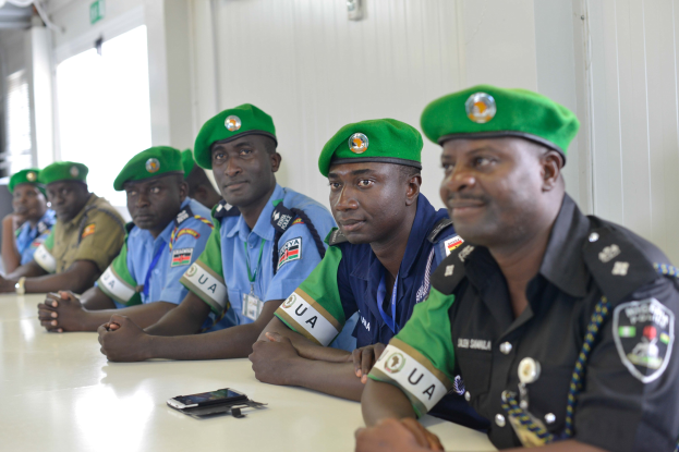 Polizisten sitzen an einem Tisch während einer Schulung, mit Mobiltelefonen und anderen Gegenständen auf dem Tisch, in einem Raum mit Fenstern und Deckenbeleuchtung.