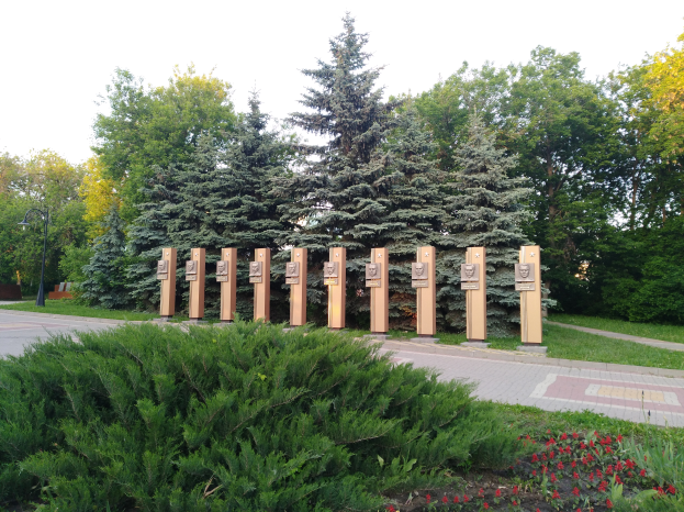 Ein Parkbild mit einem Gedenktafel für Opfer des Tschernobyl-Unfalls, umgeben von Bäumen, Blumen, Gras, einem Weg und einem Straßenmast unter einem bewölkten Himmel.