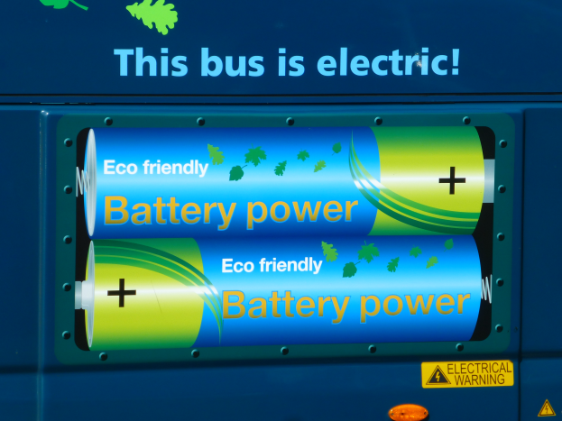 Ein blauer Elektrobus mit einer Tafel, auf der steht "Dieser Bus ist elektrisch" und zwei Batterien an der Seite.