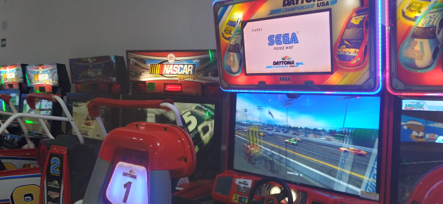 Eine Reihe buntfarbiger Arcade-Rennwagen-Maschinen in einem Raum mit einer Wand im Hintergrund.