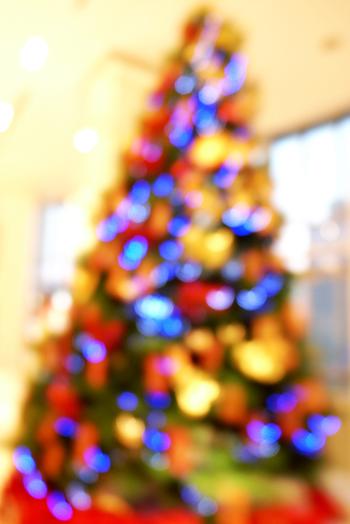 Ein unscharfer Innenraum mit einem Weihnachtsbaum in der Mitte, der mit Lichtern und Dekorationen geschmückt ist.