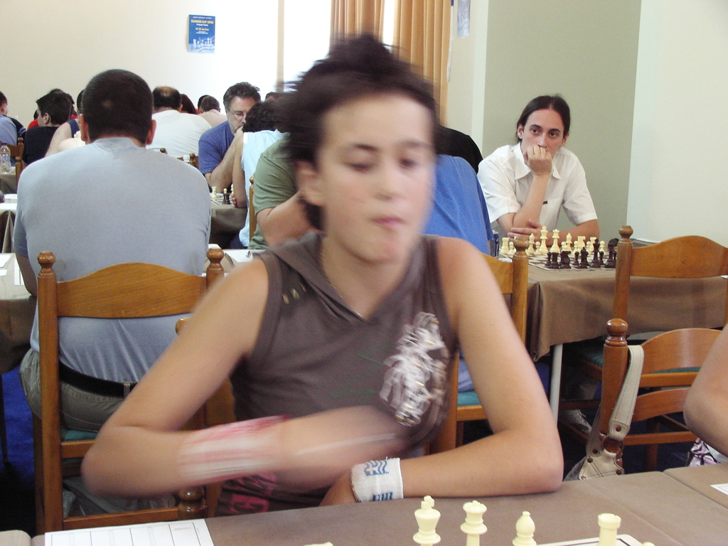 Ein Raum mit Menschen an Tischen sitzend, die Schach spielen, eine Vorhangwand mit einem Foto in der Ecke.