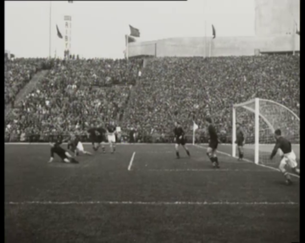 Ein Schwarz-Weiß-Foto eines Fußballspiels im Stadion, mit Spielern auf dem Feld und einem Torpfosten auf der rechten Seite, Zuschauern in den Rängen und Fahnen im Hintergrund, mit Text oben und unten: "1958-1958 WM-Endspiel - Manchester United vs. Liverpool."