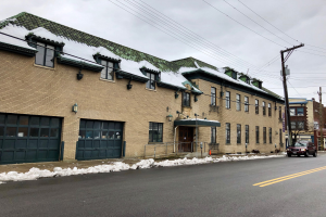 Großes Backsteingebäude mit grüner Dachfläche an einer Straßenkreuzung, umgeben von Fahrzeugen, Schnee, Strommasten, Bäumen und einem bewölkten Himmel, identifiziert als die ehemalige Feuerwache St. Louis.