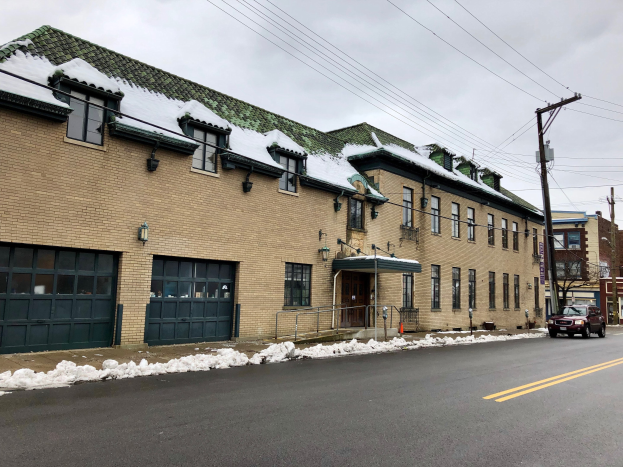 Großes Backsteingebäude mit grüner Dachfläche an einer Straßenkreuzung, umgeben von Fahrzeugen, Schnee, Strommasten, Bäumen und einem bewölkten Himmel, identifiziert als die ehemalige Feuerwache St. Louis.