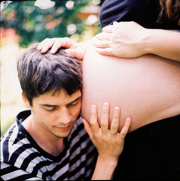 Ein Mann und eine Frau stehen nebeneinander, der Mann berührt sanft den Bauch der Frau, mit einem unscharfen Hintergrund, der das Paar und ihr ungeborenes Kind betont.