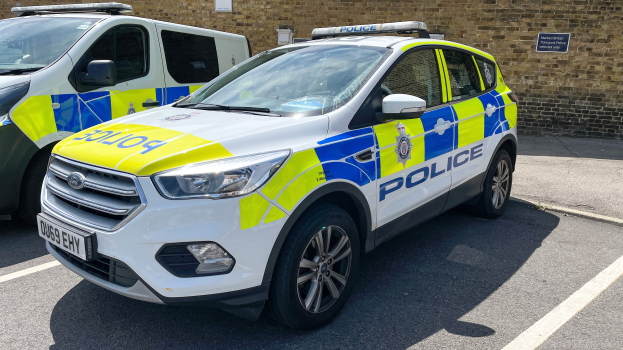 Zwei Polizeiwagen nebeneinander auf einem Parkplatz geparkt, mit einer Wand und einem Textschild im Hintergrund.