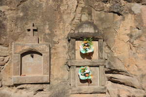 Gedenktafeln in eine Wand gemeißelt mit Blumensträußen davor.