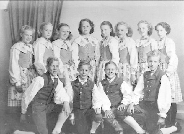 Schwarzes und weißes Foto von Kindern, die vor einer Wand mit einem Vorhang posieren, beschriftet mit "1930er Kinder-Schule" unten.