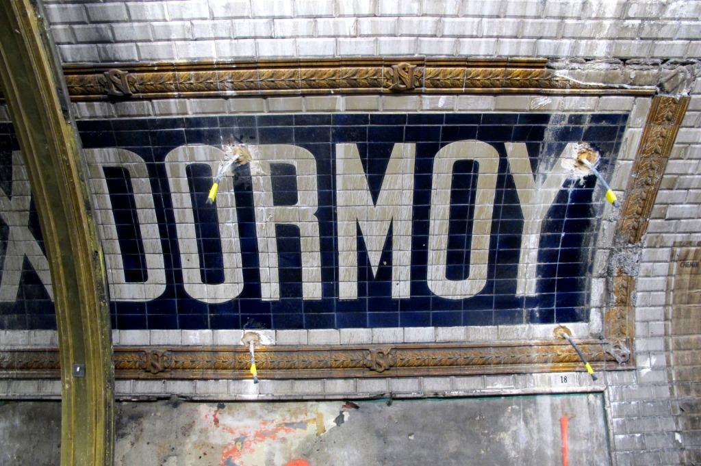 Eine U-Bahn-Station mit einem "Dormoy"-Schild an der Wand, einem Pfahl links und einer Tür unten.