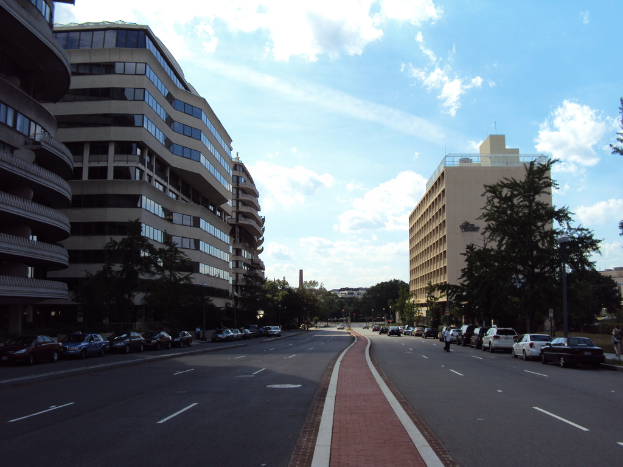 Eine Szene mit Gebäuden, Bäumen und parkenden Autos auf einer Straße.