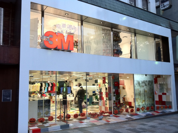 Ein Gebäude mit einer Glaswand, die Kleider auf Bügeln, eine Schaufensterpuppe, ein Fahrrad, aufgeklebte Bilder und Schrift auf dem Glas zeigt.