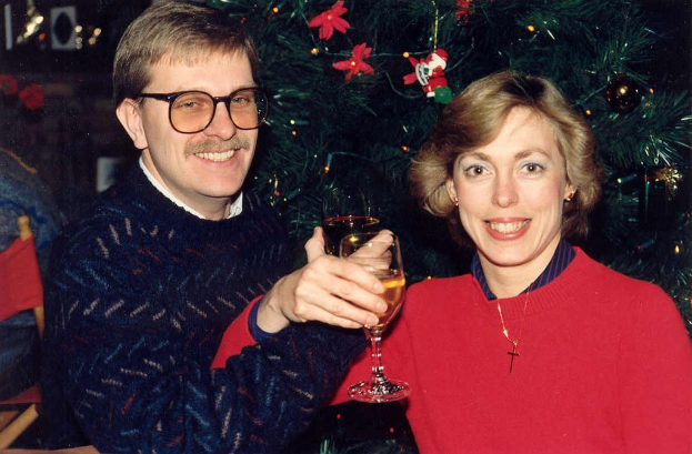 Ein Paar lächelt, waehrend es Gläser mit Wein hält, mit einem Weihnachtsbaum im Hintergrund.