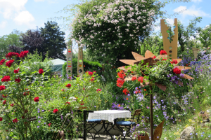 Ein Garten mit bunten Blumen und Pflanzen, der einen Tisch mit einer Decke und Stühlen zeigt, vor einem Baum und einem bewölkten Himmel auf der Chelsea Flower Show.
