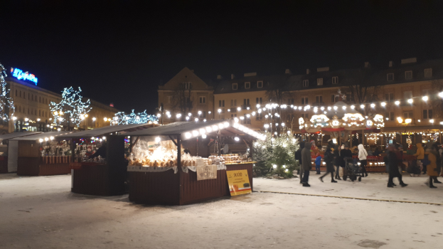 Lebendiger Weihnachtsmarkt mit Menschen, Ständen und schneebedeckter Umgebung bei Nacht.