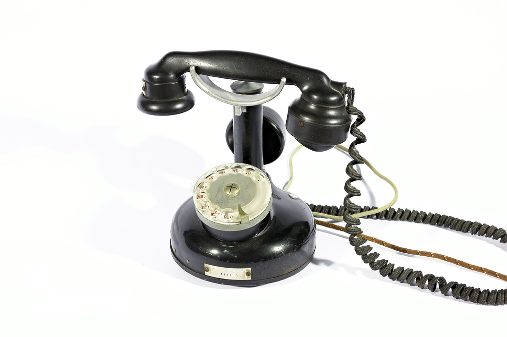 Ein schwarzes Telefon mit Zahlen und Text, der durch die Scheibe sichtbar ist, verbunden durch Drähte, vor einem weißen Hintergrund.