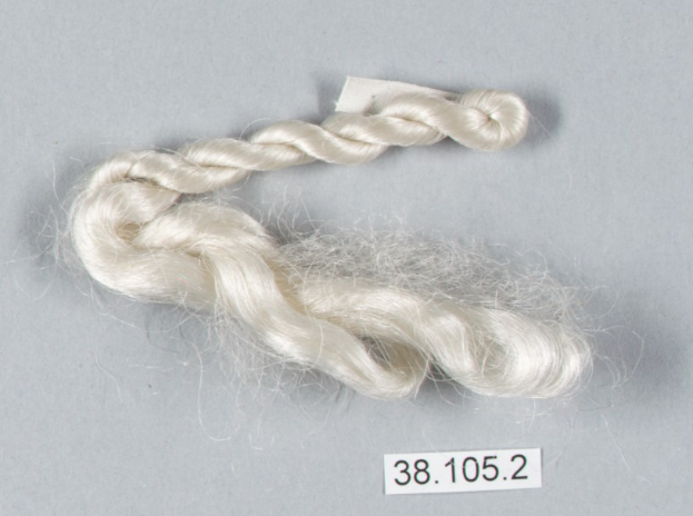 Eine Faser weißer Seidenfaden mit einer Zahl darauf, die auf einer grauen Oberfläche liegt.