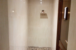 Ein Badezimmer mit einer Walk-in-Dusche, Toilette und Tür auf der rechten Seite, mit Fliesen an den Wänden und Deckenleuchten.