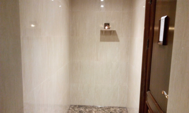 Ein Badezimmer mit einer Walk-in-Dusche, Toilette und Tür auf der rechten Seite, mit Fliesen an den Wänden und Deckenleuchten.