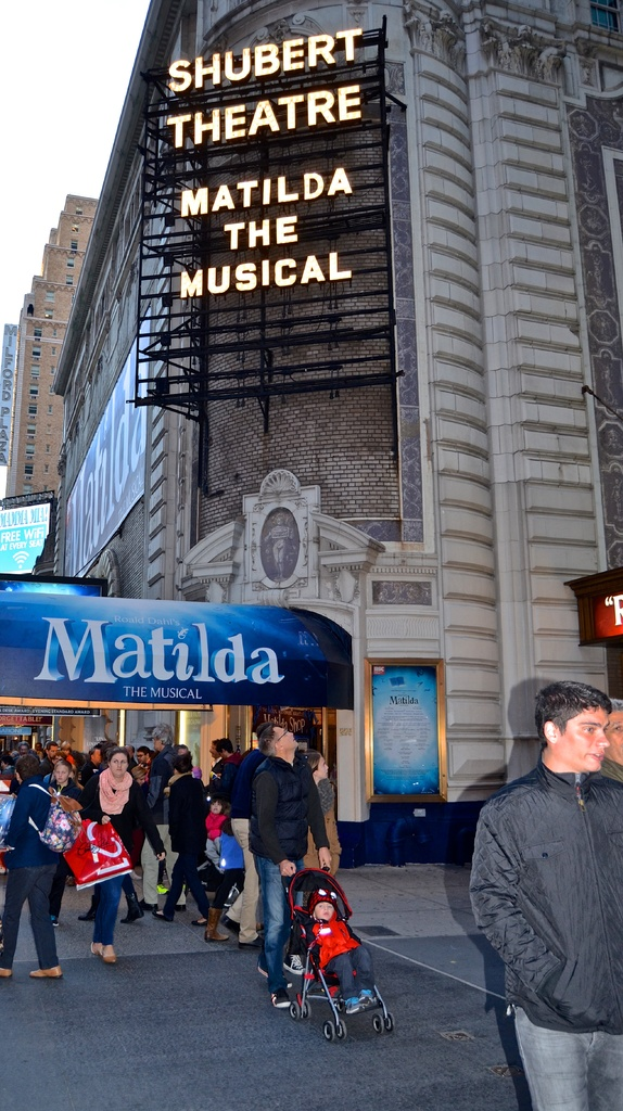 Eine Gruppe von Menschen in der Nähe von Gebäuden und Bauzäunen mit einem Baby im Kinderwagen.