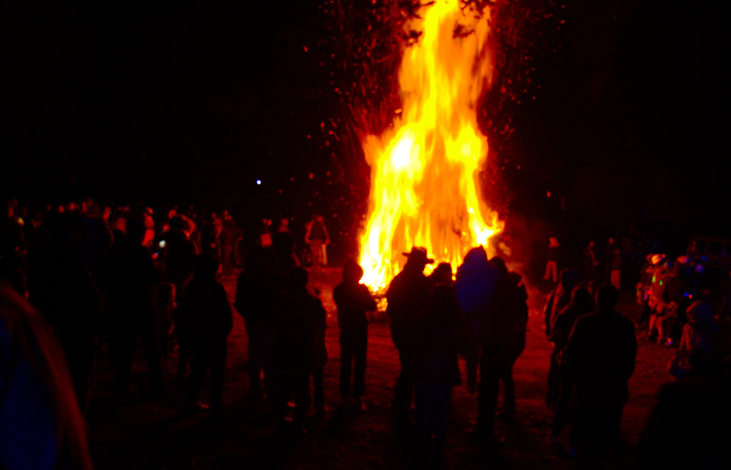 Eine Gruppe von Menschen steht mit einem Feuer im Hintergrund.