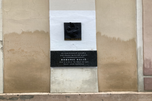 Schwarze Tafel an einem Gebäude mit einer darauf liegenden Hand, mit Inschrift, wahrscheinlich ein Holocaust-Mahnmal.