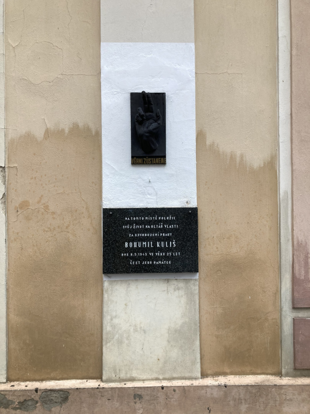 Schwarze Tafel an einem Gebäude mit einer darauf liegenden Hand, mit Inschrift, wahrscheinlich ein Holocaust-Mahnmal.