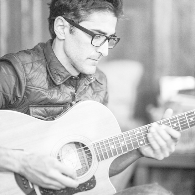 Ein Mann in einer Jacke, der eine Gitarre spielt.