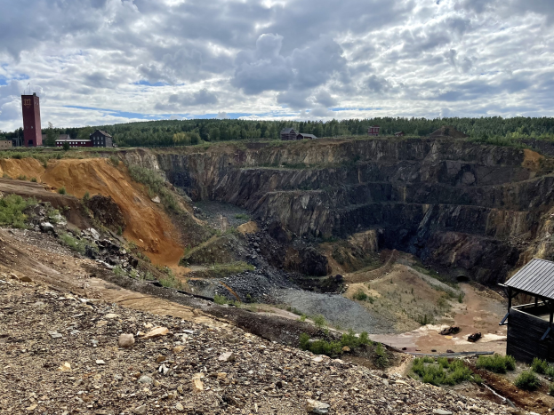 Großer Tagebau in einer Schotterfläche umgeben von Bäumen, Gebäuden und einem Schuppen.