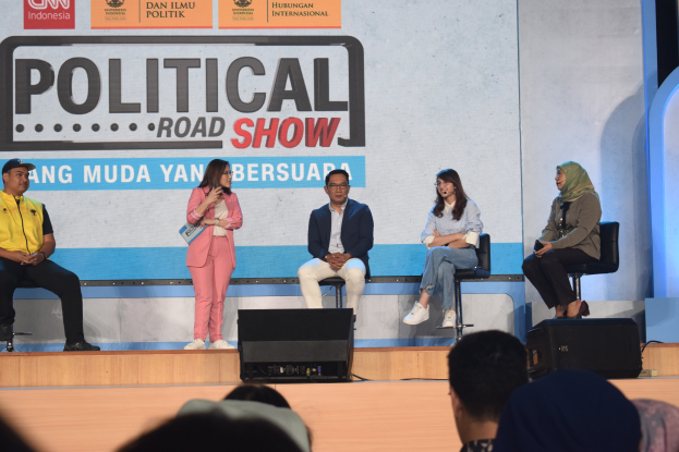 Eine Gruppe von Menschen auf einer Bühne mit einer Frau, die ein Mikrofon hält, vorne eine Zuschauermenge und im Hintergrund eine Wand mit der Aufschrift "Politischer Roadshow 2019".