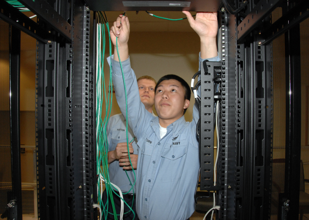 Zwei Männer arbeiten an einem Server in einem Rechenzentrum, umgeben von Kabelregalen und einer Wand im Hintergrund.