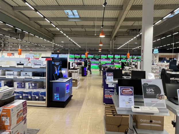 Großer Raum in einem Walmart-Laden voller Elektronik, die in Regalen angeordnet ist, einschließlich Computer und Drucker, mit Menschen auf dem Boden, einer Säule, Schildern, Deckenleuchten und Deckenventilatoren.