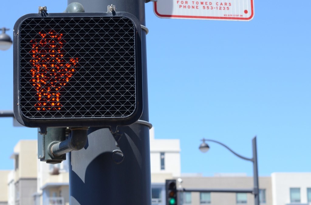 Eine Straßenszene in der Stadt mit Verkehrspfosten, Ampeln, Laternen, Gebäuden und einem klaren Himmel.