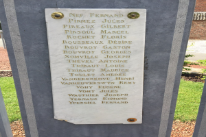 Steinbank mit Gedenktafel vor einem Backsteingebäude, umgeben von Grün.