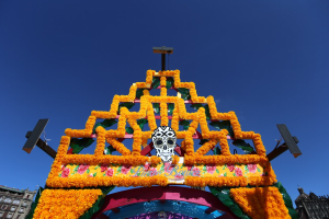 Ein Día de los Muertos-Bogen, geschmückt mit Blumen und einem Schädel, steht in Mexiko-Stadt vor Gebäuden unter einem klaren blauen Himmel.