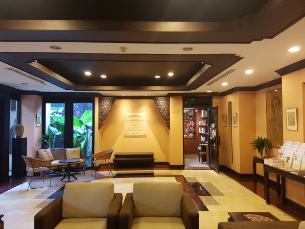 Ein Hotellobby mit Sitzbereichen, Tischen, Zimmerpflanzen, Bücherregalen, Leuchten, Wandschmuck und Beistelltisch-Dekoration, mit natürlichem Licht von Fenstern und Türen.