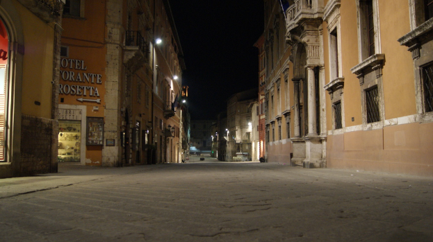 Stadtansicht bei Nacht mit Gebäuden auf beiden Seiten, einem Schaufenster auf der linken Seite und Straßenlaternen, die die Mitte der Straße beleuchten.