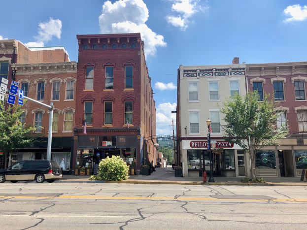 Eine Stadtstraße mit parkenden Autos, Gebäuden, Bäumen, Laternen, Schildern und einem Feuerhydranten unter einem bewölkten Himmel, repräsentiert eine kommerzielle Immobilie zum Verkauf.