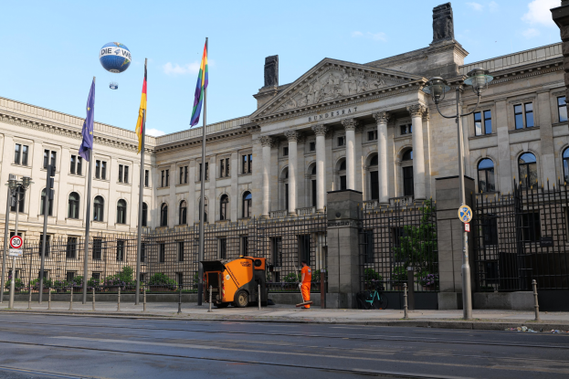 Großes modernes Gebäude mit zahlreichen Fenstern, identifiziert als der Bundestag in Berlin, Deutschland, umgeben von Straßeninfrastruktur, Fußgängern, Fahrzeugen und Bäumen unter einem bewölkten Himmel.