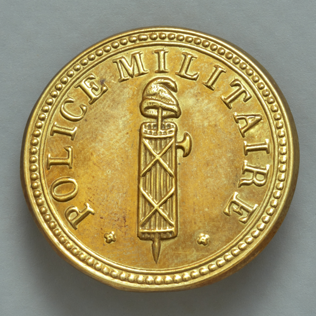 Eine Goldm├╝nze mit der Aufschrift "Police Militaire" vor einem wei├čem Hintergrund.