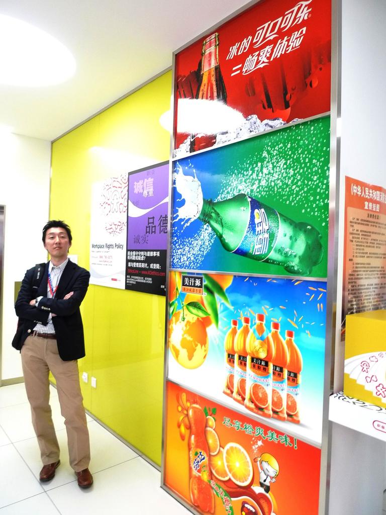 Ein Mann im Blazer steht vor einer Wand mit Softdrink-Werbung.