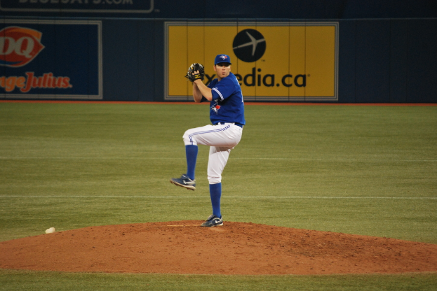 Ein Spieler steht auf dem Boden und hält einen Ball in der Hand, im Hintergrund ist ein großes Banner mit Text und Bildern zu sehen.