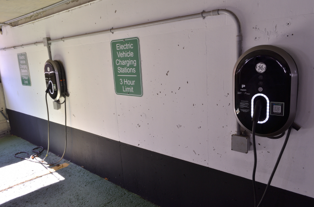 Eine Ladeeinrichtung für Elektrofahrzeuge in einer Tiefgarage mit zwei wandmontierten Ladegeräten und Informationsschildern, wobei der Boden unten zu sehen ist.