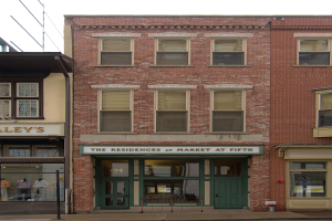 Ladenfront von "Residences at Market at Fifth" mit Glasfenstern und -türen, Schaufensterpuppen in Kleidern, einer Straße darunter und Himmel im Hintergrund.