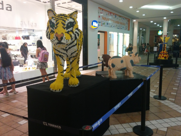 Tierstatuen auf schwarzen Kisten umgeben von Pfählen mit Gummibändern, mit Geschäften, die Taschen, Schuhe und andere Artikel anbieten, und Menschen, die herumlaufen.